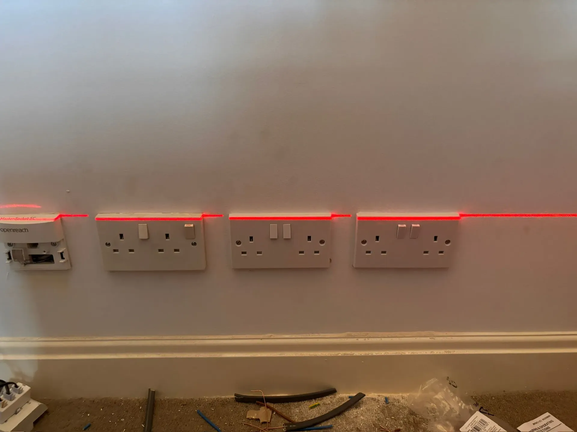 Electrician using a red laser level to perfectly align new double power sockets and a data socket on a wall.